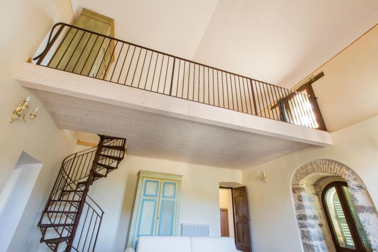 Interno di un appartamento con soppalco e una scala a chiocciola, situato in un borgo immerso nel verde.