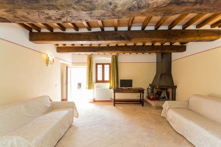 Ampio soggiorno con travi in legno e camino. Spazio adatto per momenti di relax con vista sulla campagna.