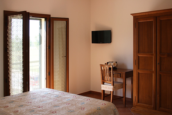 Camera semplice con letto matrimoniale, tavolo e panorama sulla campagna circostante.