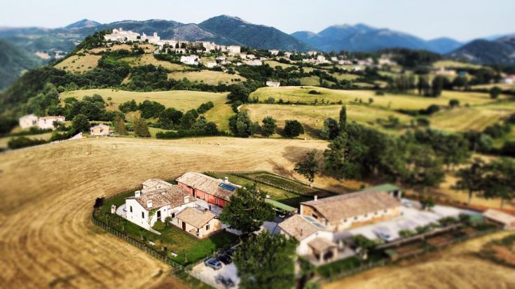 Scena di un agriturismo circondato da colline verdi e campi coltivati.