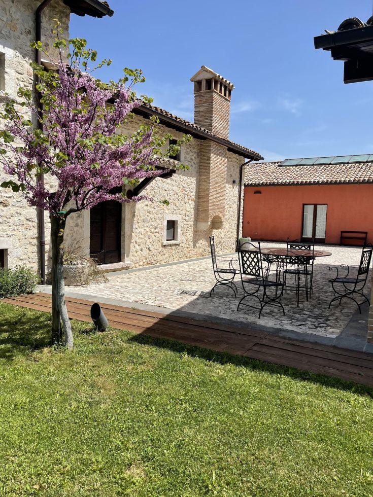 Un ambiente esterno curato con un albero in fiore, tavoli e sedie immersi nella natura.