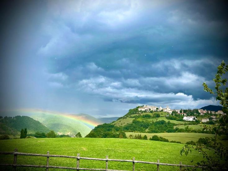 Un paesaggio naturale con un arcobaleno che si erge sopra le colline, visibile dal villaggio circostante.