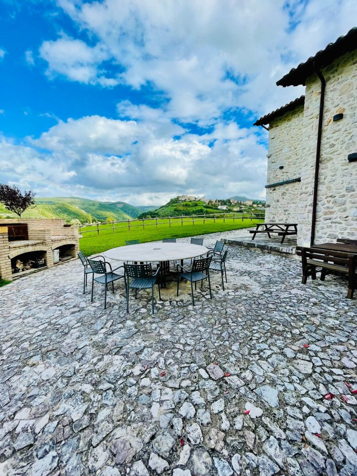 Un patio esterno con spazio per rilassarsi, circondato da verdi colline e un cielo sereno.