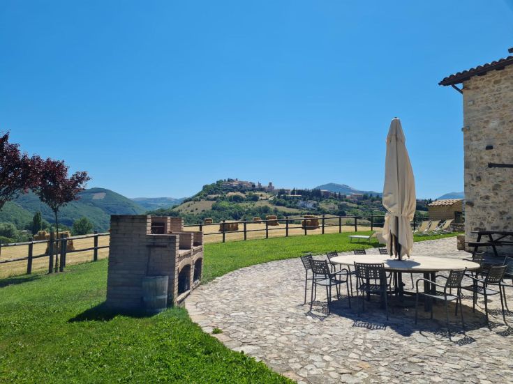Un'area serena di un agriturismo con panorama su colline verdi e cielo azzurro.