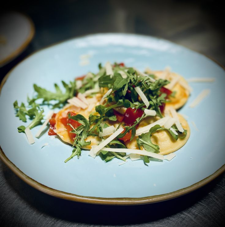 Ravioli conditi con pomodorini, rucola e scaglie di formaggio.