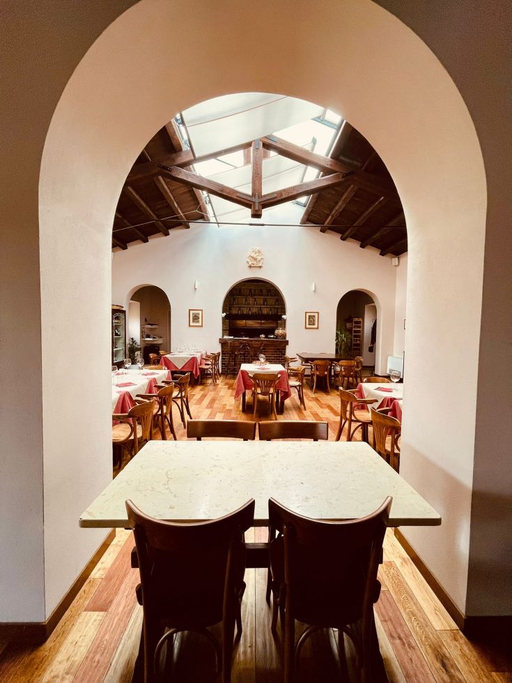 Interno di un ristorante con tavoli apparecchiati e soffitti alti, illuminato da luce naturale.