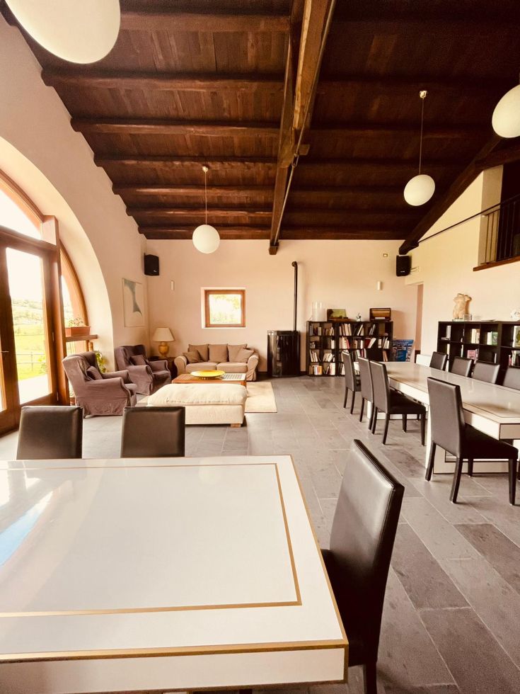Un ampio spazio interno caratterizzato da travi in legno e un grande tavolo centrale per accogliere ospiti.