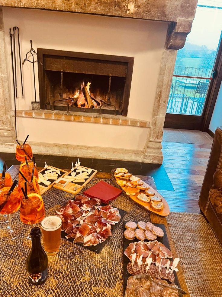 Un ambiente tranquillo con salumi, snack e bevande disposti vicino a un camino acceso.