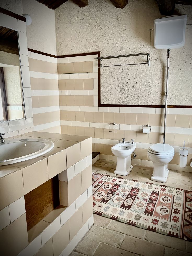 Un bagno sobrio e confortevole con piastrelle chiare e un tappeto dai toni vivaci.