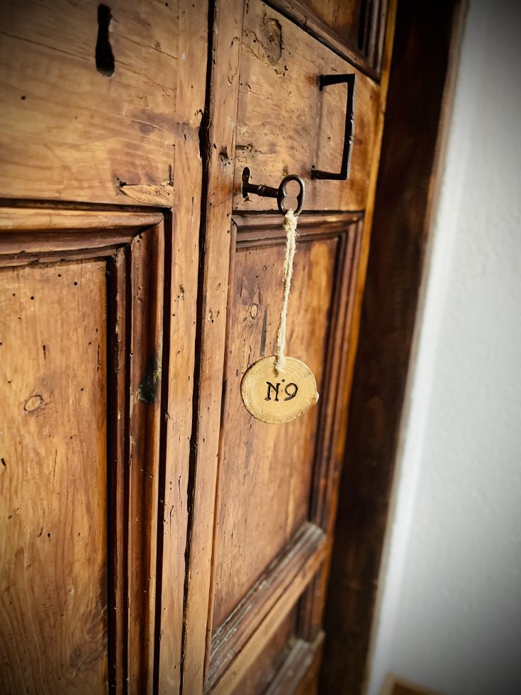 Particolare di un armadio in legno con chiusura a chiave e un elemento identificativo.