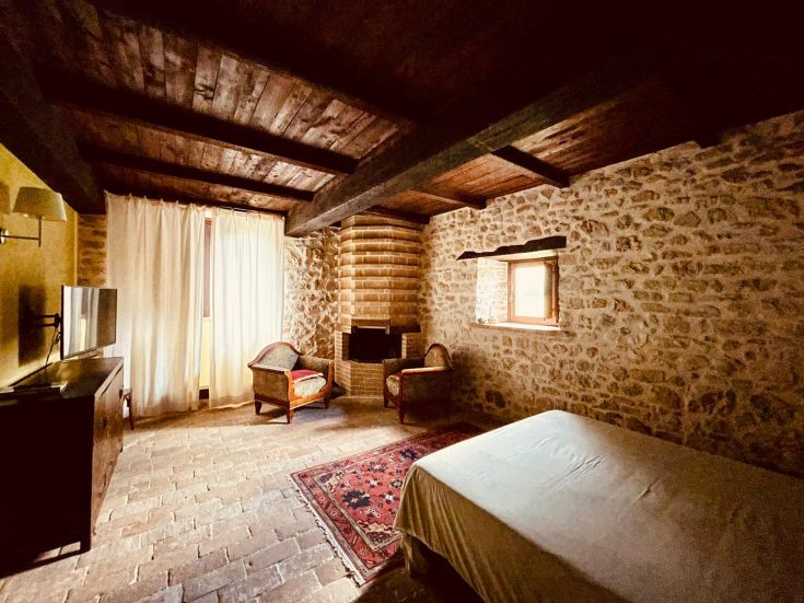 Interno di una camera con pareti in pietra e arredamento semplice e rustico.