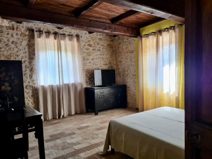 Camera semplice in agriturismo con pareti in pietra e tende legate al soffitto.