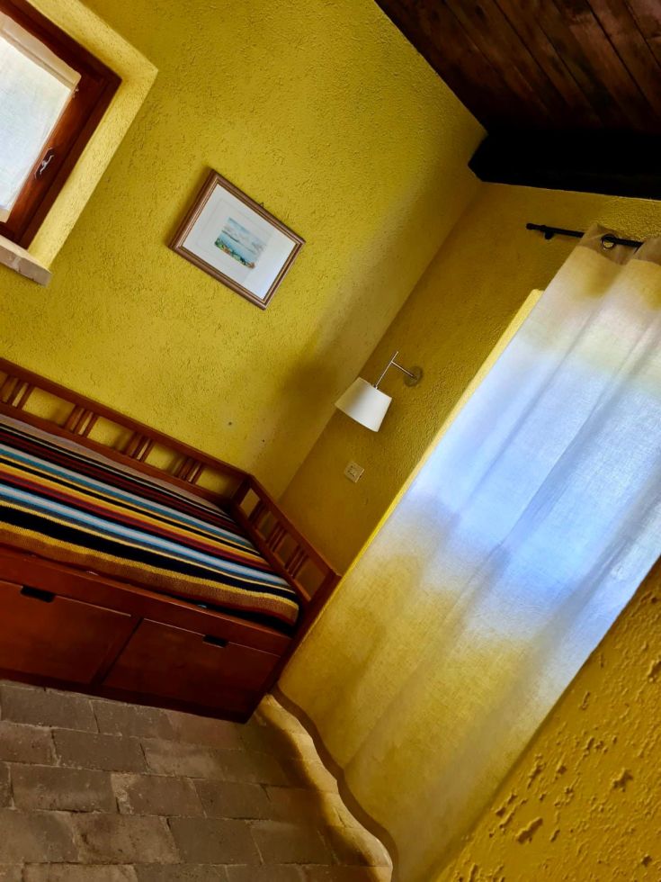 Una stanza spaziosa con pareti gialle e un letto dai colori vivaci, illuminata da luce naturale.