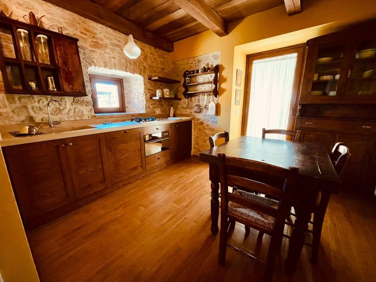 Cucina semplice con finiture in legno e pietra, illuminata dalla luce del sole.