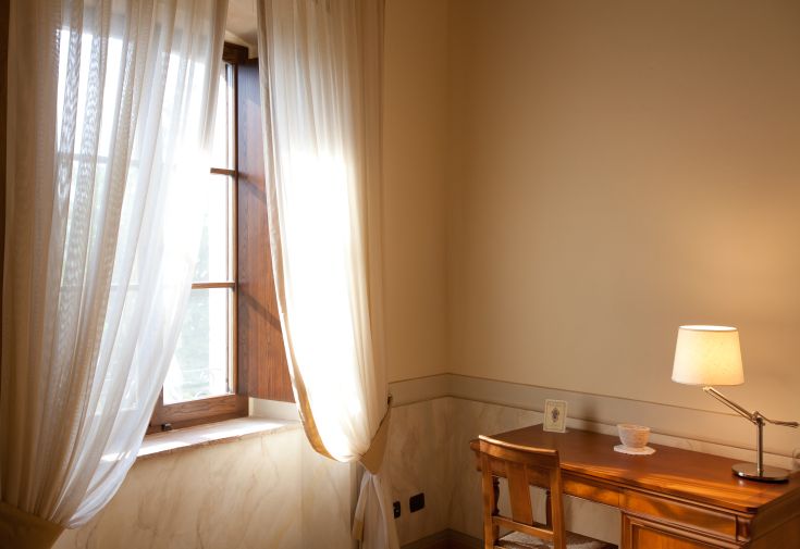 A simple interior with soft lighting, featuring a lamp and a wooden table, surrounded by light curtains.