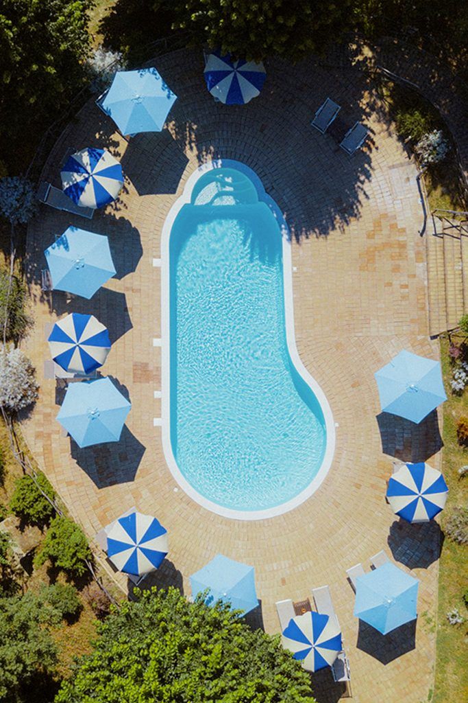 A pool with blue and white umbrellas, surrounded by greenery, perfect for relaxation.