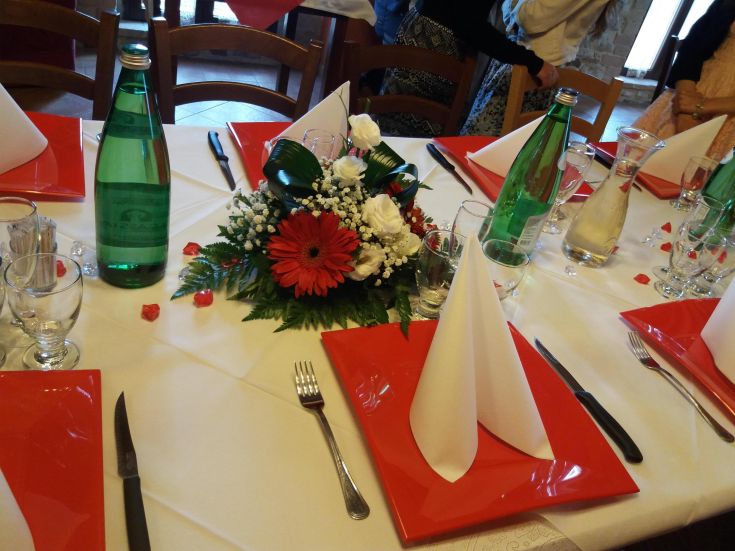 Ein einfach gedeckter Tisch mit einem weißen Tischtuch, roten Tellern und einem Blumenmittelstück.