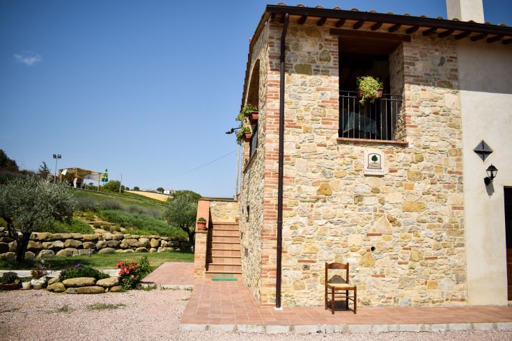 Ein Steinhaus mit architektonischen Elementen, die harmonisch in die Umgebung integriert sind, mit einem Stuhl im Freien, umgeben von Pflanzen.