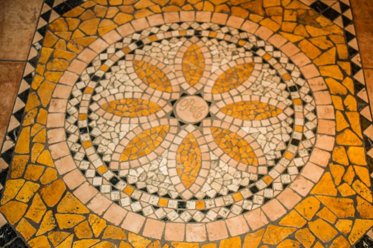 Ein dekoratives Mosaik mit floralen Mustern und warmen Farben, das harmonisch in die Umgebung integriert.