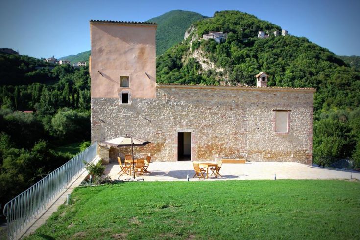 A historic stone building surrounded by lush greenery, reflecting the Umbrian character.