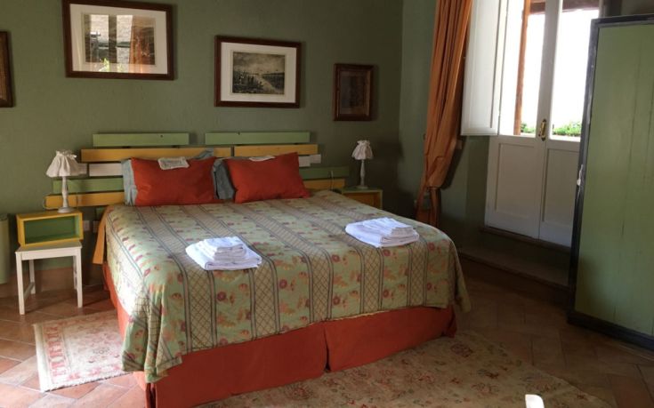 Ein einfaches Zimmer mit einem Doppelbett, in warmen Tönen dekoriert und mit Blick auf einen grünen Garten. Eine ruhige Umgebung.