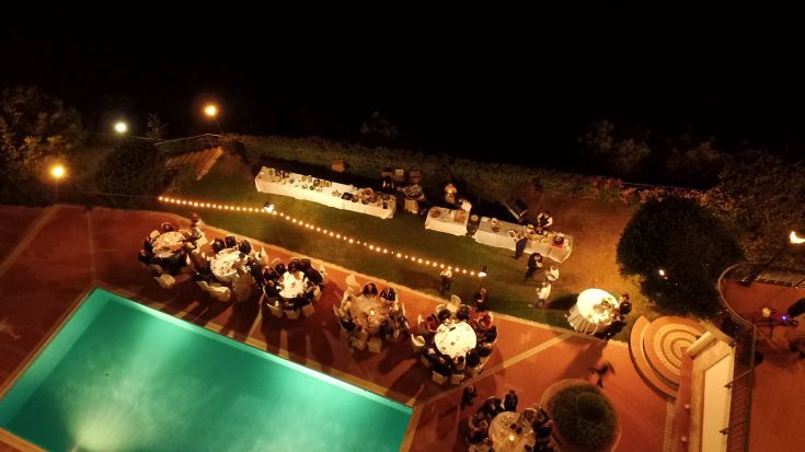 An evening reception by a pool surrounded by simple tables and understated decorations.