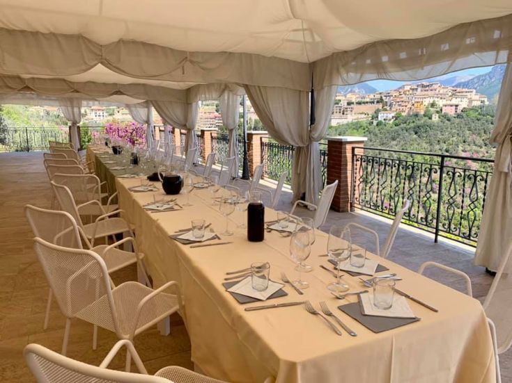 An outdoor set table surrounded by plants, overlooking gentle hills.