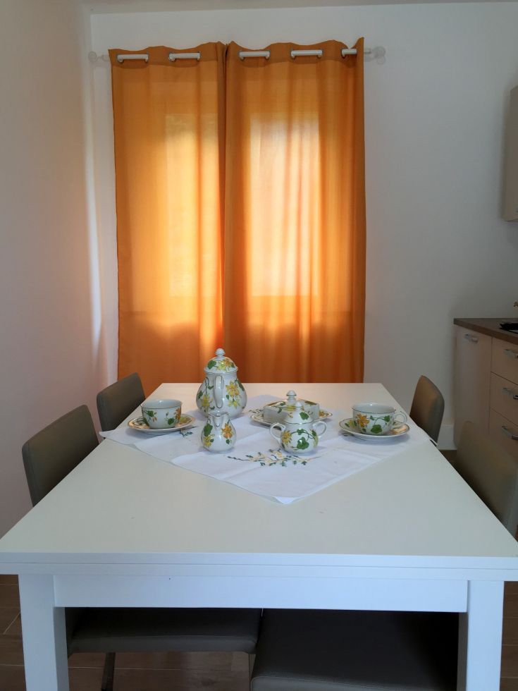 Una cucina ben illuminata con una tenda arancione e un servizio da tè posato su un tavolo bianco.