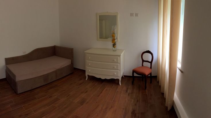 Un ambiente sobrio e accogliente con un divano, un mobile comò e una sedia in un angolo ben illuminato.