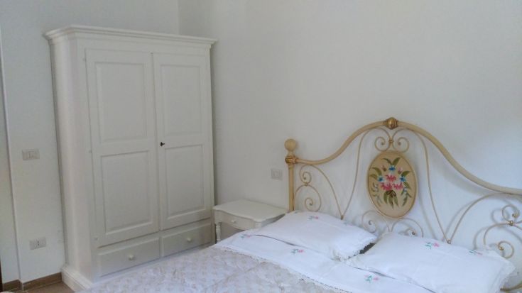 Camera semplice con letto matrimoniale e armadio bianco, circondata dalla quiete e dal verde.