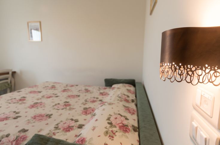 Camera semplice con letto a tema floreale e lampada sottile, ideale per un soggiorno tranquillo.