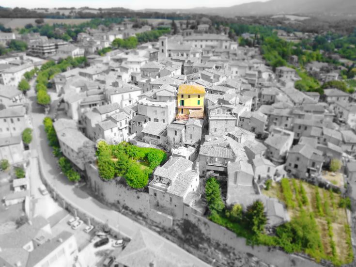 Luftaufnahme eines mittelalterlichen Dorfes mit einem auffälligen gelben Haus zwischen den Dächern.