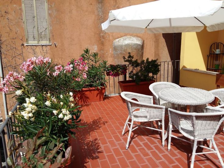 Helle Terrasse mit weißen Tischen und Stühlen, geschmückt mit bunten Blumen und umgeben von alten Mauern.