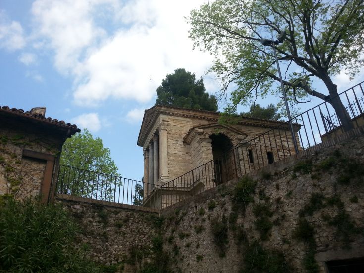 Scene of the Tempietto del Clitunno surrounded by typical Umbrian trees and vegetation, showcasing style and history.