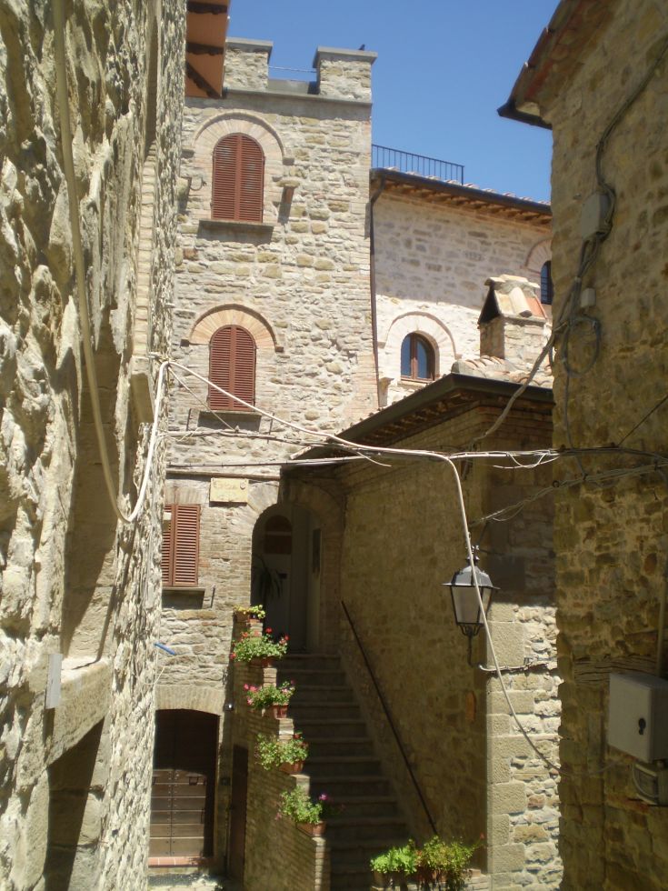 Eine ruhige Straße in einem charmanten umbrischen Dorf mit Steinbauten und Blumen an den Seiten.