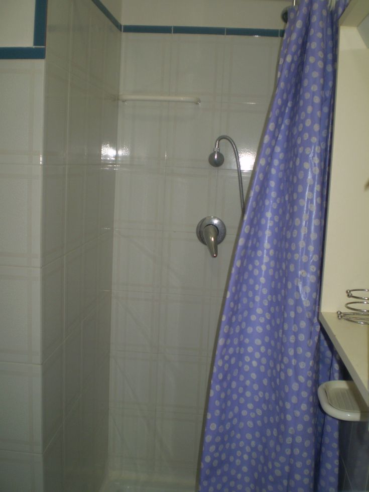 Einfach gestaltete Dusche mit hellen Fliesen und blauen Punktvorhängen.