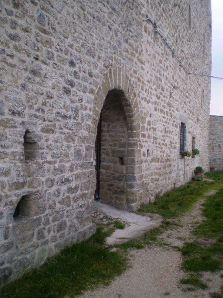 Ein Steinbogen führt zum Eingang eines ländlichen Gebäudes, umgeben von Grünflächen.