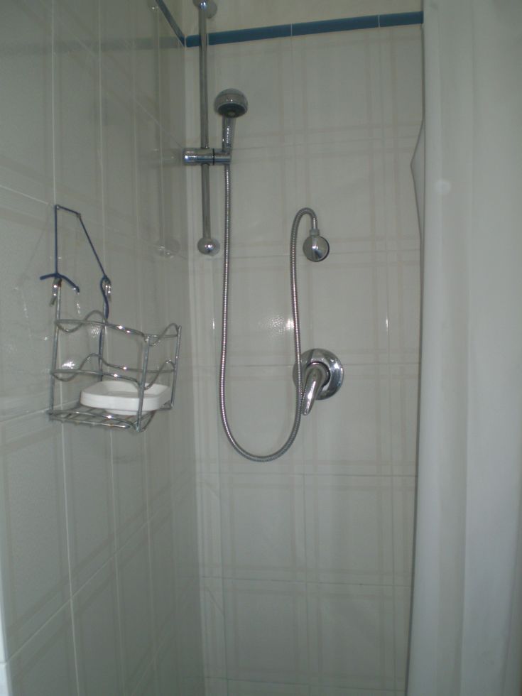 Innenansicht einer Dusche mit Duschkopf, Wasserhahn und Seifenspender.