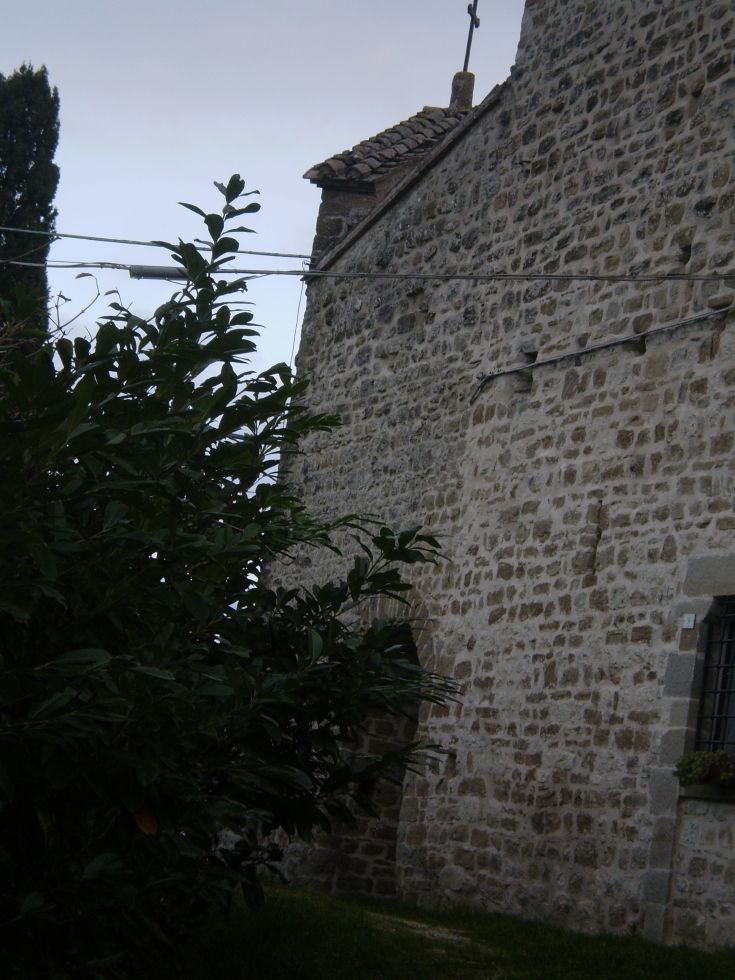 Seitenansicht eines steinernen Gebäudes, umgeben von Grün, in einer ruhigen und rustikalen Umgebung.