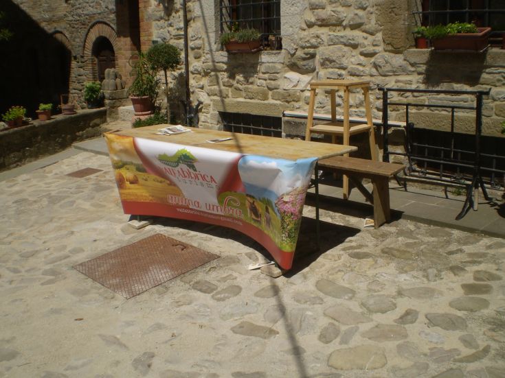 Ein Werbetisch im Freien mit einem Banner, umgeben von Grün und einer Steinmauer.