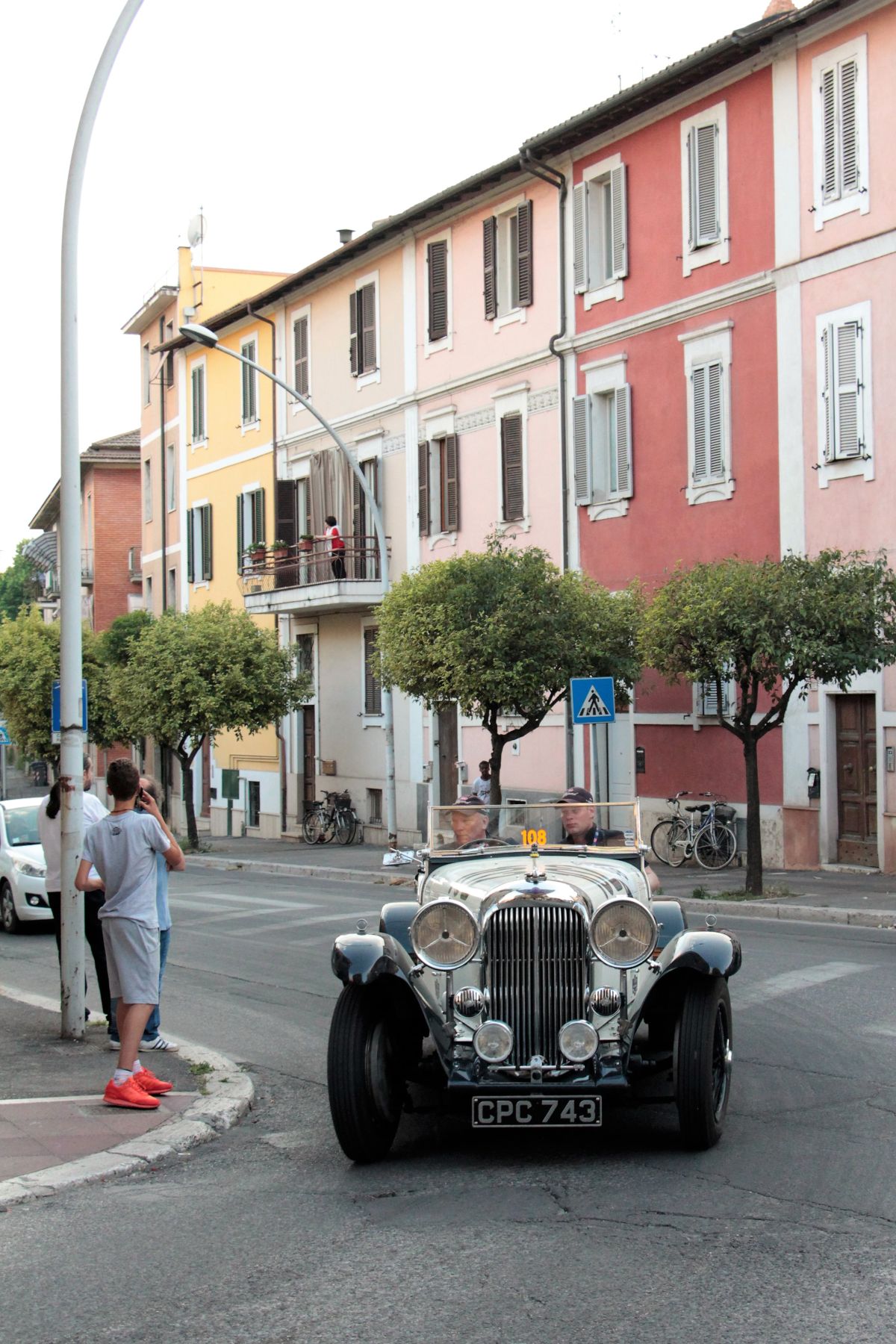 A vintage car drives along a street adorned with colorful building facades.