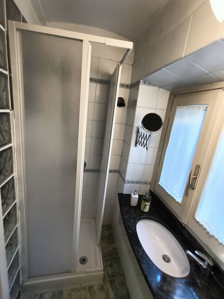 Salle de bain simple avec douche, lavabo et miroir, aménagée de manière pratique.