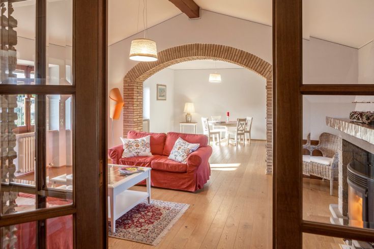 Ambiente confortevole e luminoso di un soggiorno in un casale, con un divano rosso e un tavolo da pranzo in legno.