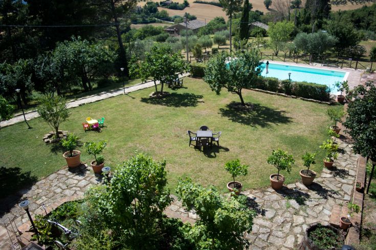 Un giardino spazioso con piscina circondato da alberi e piante tipiche della campagna umbra.