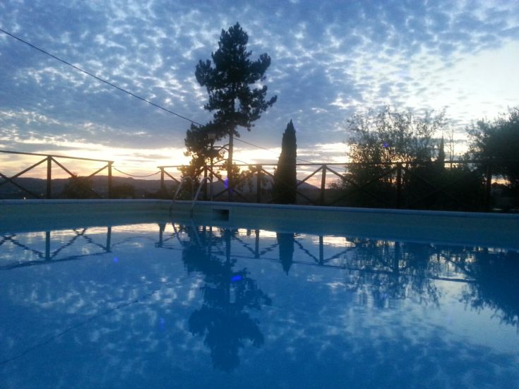 Scena di una piscina al tramonto, con riflessi e tonalità che si fondono con l'ambiente circostante.