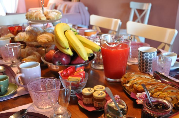 A table set with various foods: croissants, fresh fruits, and assorted drinks.