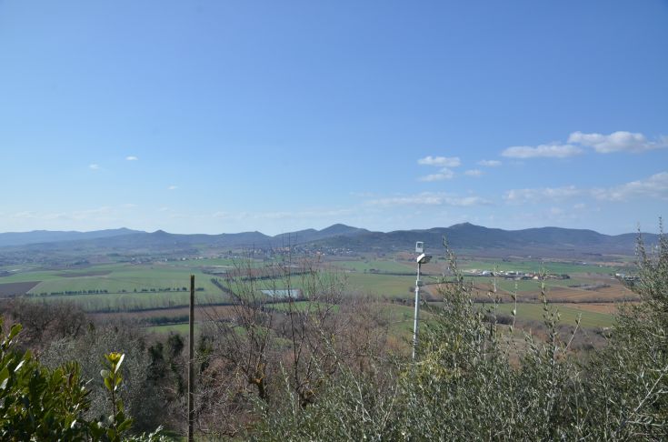 A panoramic view over green hills and mountains under a clear sky.