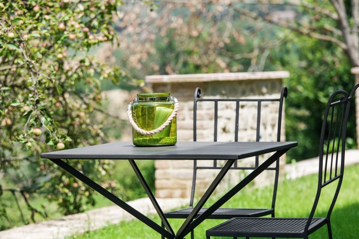 Un tavolo in metallo si trova in un giardino ben illuminato, decorato con un vaso verde.