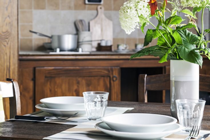 Un tavolo semplicemente allestito con piatti e bicchieri, inserito in un ambiente confortevole.