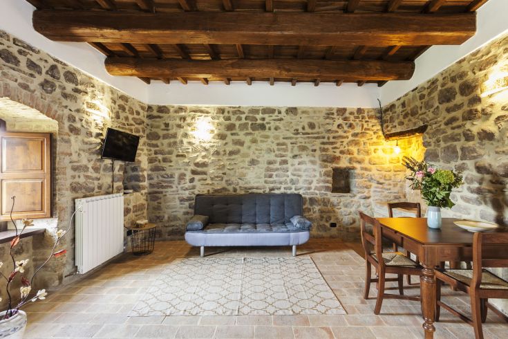 Ambiente rilassato con pareti in pietra, travi di legno a vista e un'atmosfera calda e semplice.